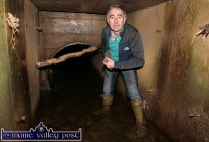 Cllr. John Joe Culloty pictured at the joint of the culvert under the road at Tullig where the pipe-size drops to half capacity. The branch jammed in the flange and the debris caught on the shuttering clips add their own chapters to the bigger flooding story. ©Photograph: John Reidy